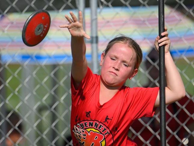 A female Bennett Blazers athlete throws a discus during a track and field event.