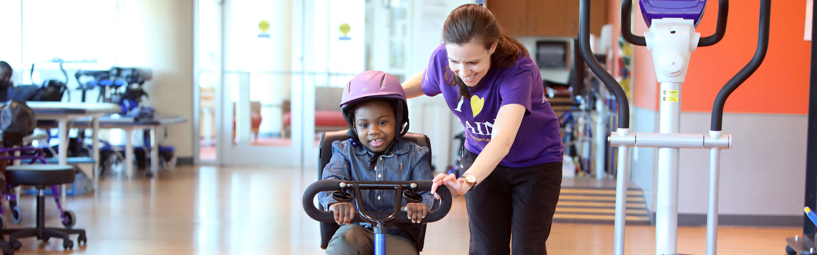 Journee, a patient at Phelps Center, rides a bike with the assistance of her therapist.