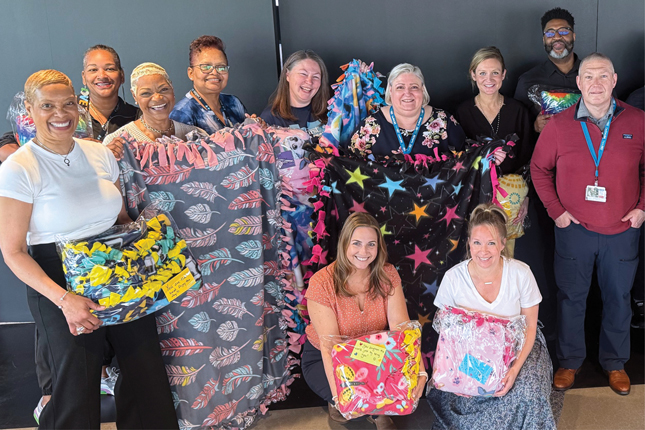 CareFirst employees smile as they hold no-sew blankets made for Kennedy Krieger patients.