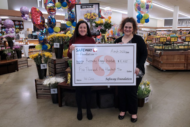 Two women smile inside a Safeway as the Safeway Foundation presents a ceremonial check to Kennedy Krieger.