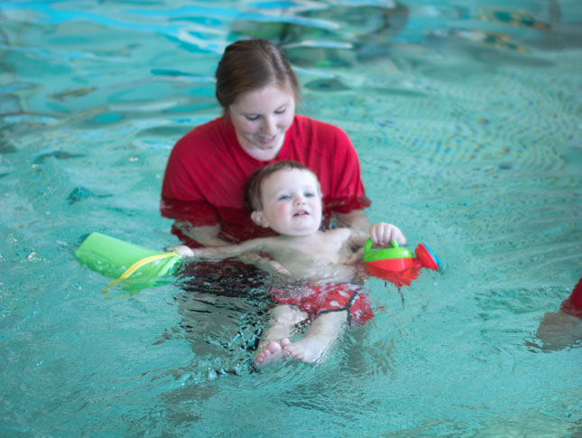 A female therapist aids a young boy during a session in a pool.