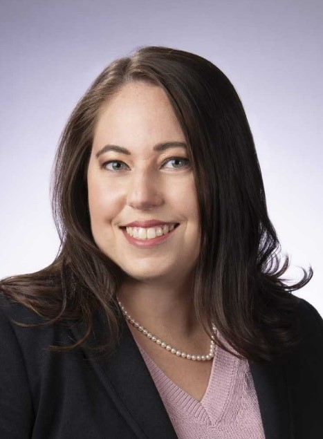 Professional headshot-style photo of a woman smiling and wearing a pink sweater and black suit jacket.