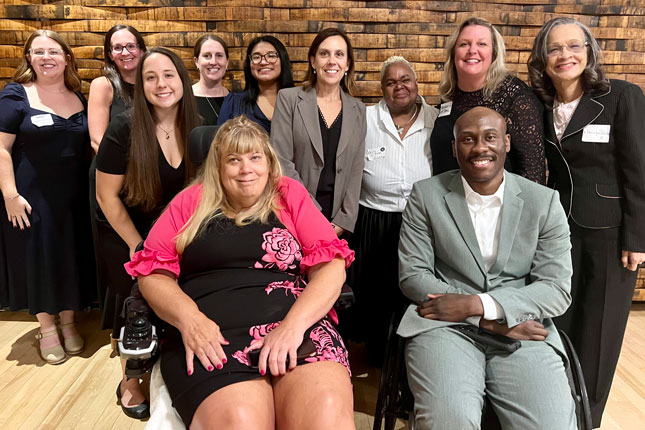 A large group of people in professional attire gather for a photo at Disability Rights Maryland’s Breaking Barriers Awards Gala. A man and woman in the front are sitting in mobility devices while the rest of the group stands behind them.