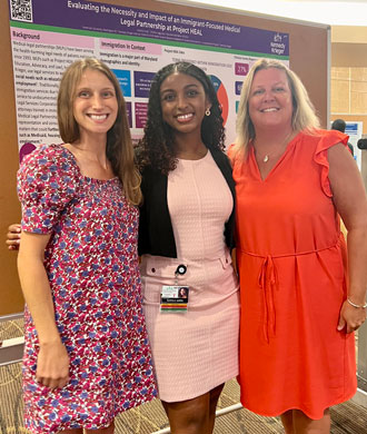 Three women stand in front of a research poster and smile.