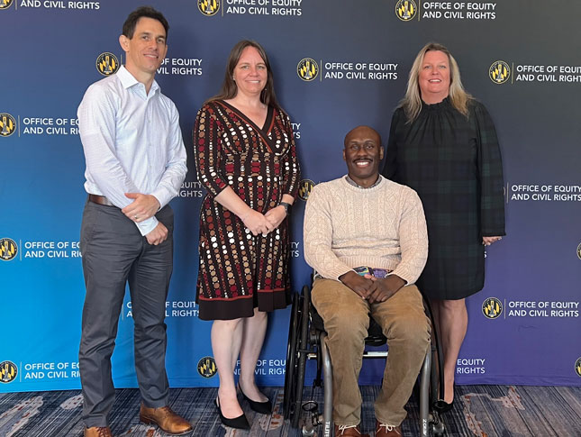 David Mervis, Genevieve Hornik, Chris Mason-Hale and Maureen van Stone pose for a photo in front of a step and repeat banner at Mayor’s Commission on Disabilities Breakfast.