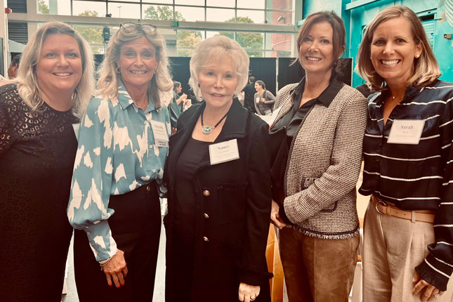 Five women stand next to each other for a photo and smile.