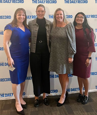 Kendall Eaton, Genevieve Hornik, Cindy Ibarra and Maureen van Stone stand in front of a Daily Record step and repeat banner.