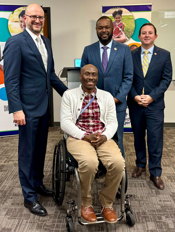 Chris Mason-Hale, Kennedy Krieger president and CEO Brad Schlaggar, Maryland state senator Cory McCray and Maryland senate president Bill Ferguson. Mason-Hale is sitting in his mobility device as the others stand behind him.