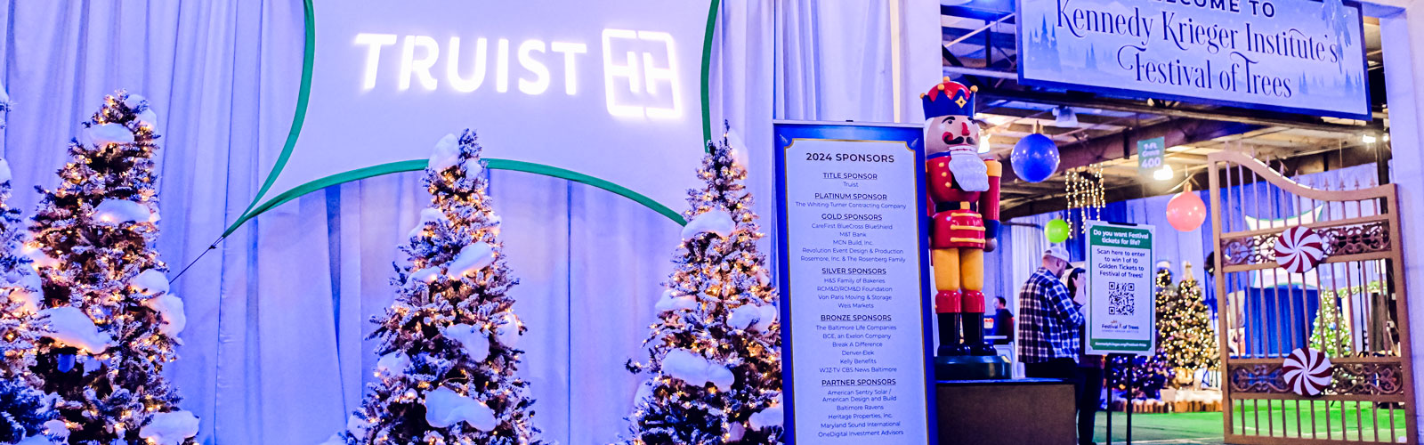 A Truist banner hangs above a lighted grove of trees, a pull up banner listing all 2024 sponsors and a large nutcracker.