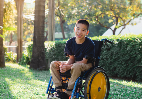 A young boy sits in a wheelchair smiling. 