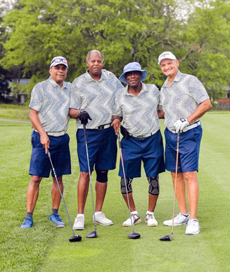 Four golfers smile in a group photo on the course.