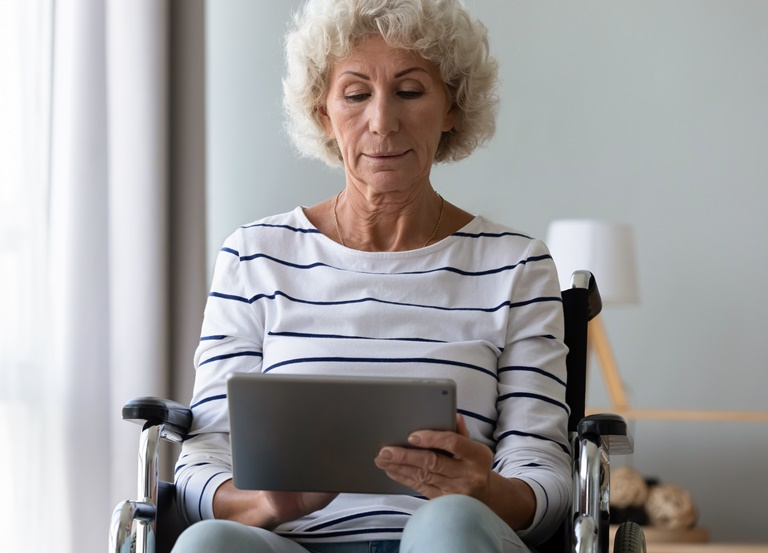 A female patient using a wheelchair holds a tablet in her home