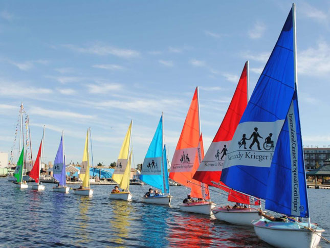 A line of boats in Baltimore's Inner Harbor featuring colorful sails with the Kennedy Krieger Institute logo.