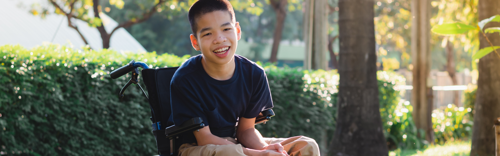 A young boy sitting in a mobility device smiles.