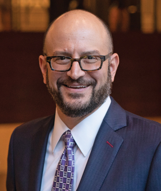 A professional headshot-style photo of a man wearing a suit and tie.