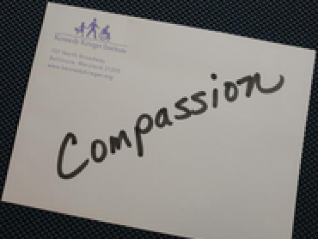 A piece of paper with the word "Compassion" written across it in black