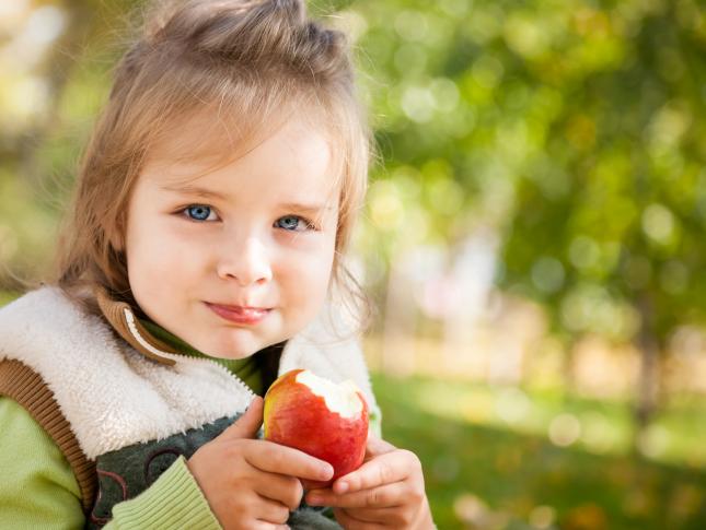 A young girl is holding an apple she has taken a bite out of while sitting outside