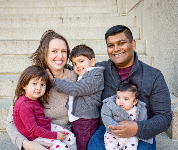 A family portrait of a mother and father, with a little boy and girl, and a baby girl. Everyone but the baby is smiling.
