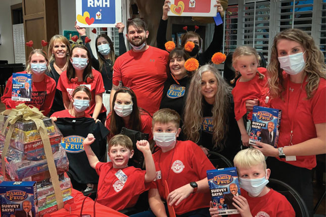 A group of children and adults pose for a photo at Ronald McDonald House. Most of them are wearing red t-shirts.