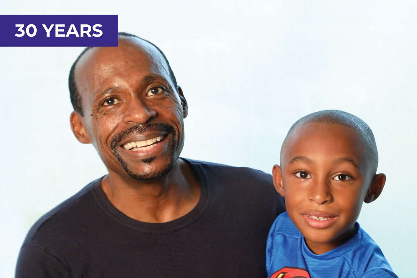 A father and son smile for the camera. The son is about 5 years old and appears to be wearing a Superman T-shirt.