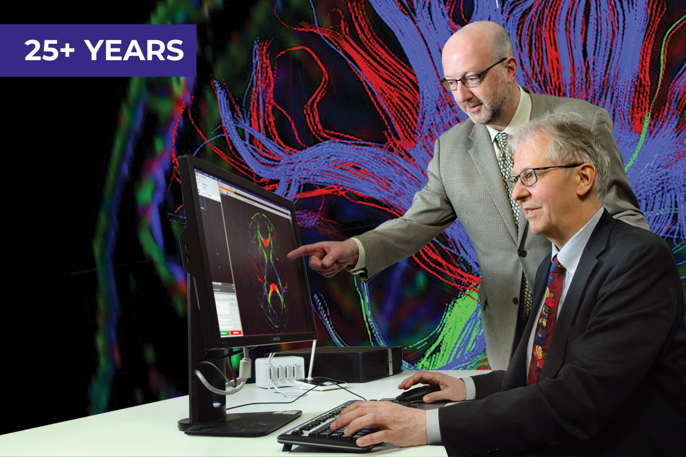 Two men in business suits work at a computer, which displays a colorful MRI image of a human brain.