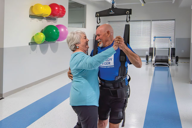 A woman and a man share a dance in a gym setting. The man is in a harness that is attached to the ceiling and holding him up.