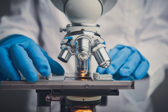 Two latex-gloved hands operate a microscope.