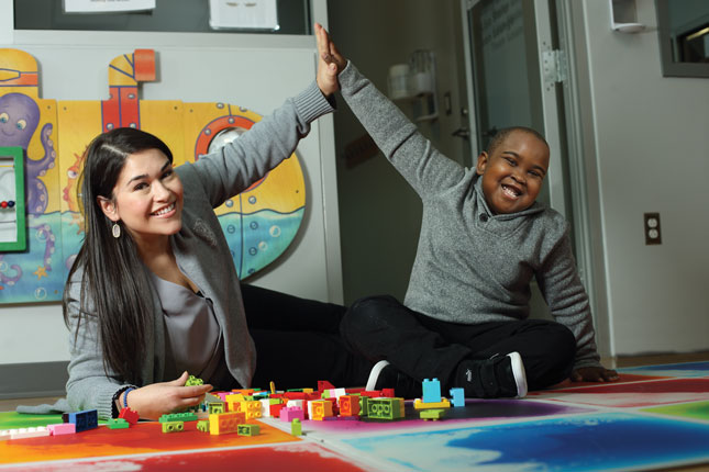 A teacher and a young boy high-five each other while playing with Lego bricks.