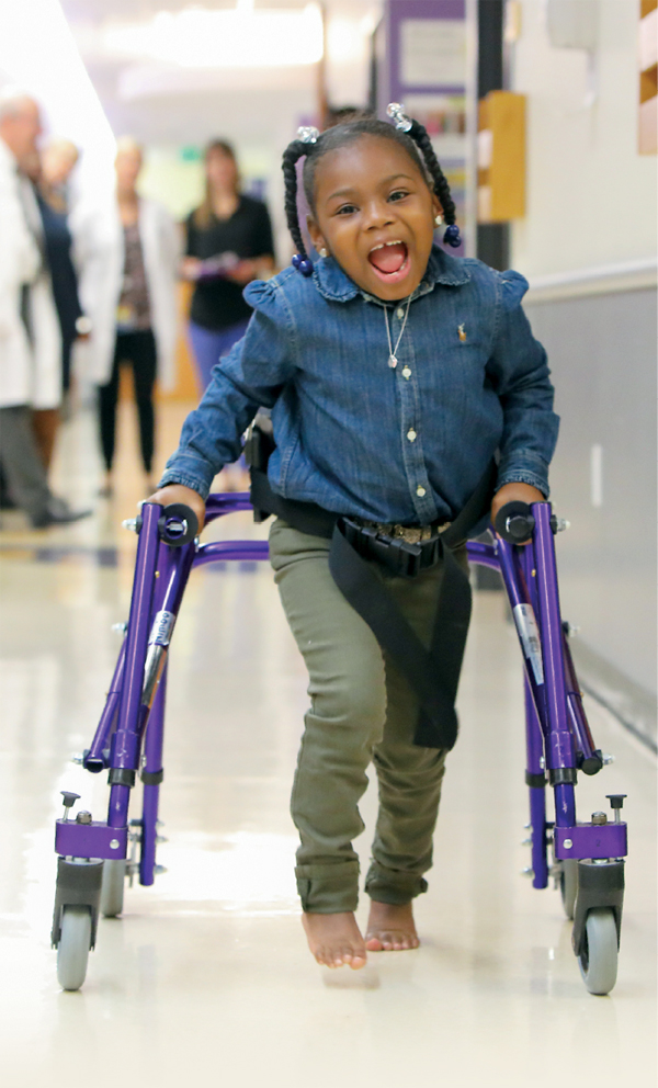 A photo of Journee walking down a hallway at Kennedy Krieger while using her walker.