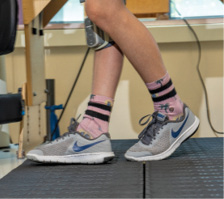 A photo of Brayden's legs as he uses a Bioness device while walking on a treadmill during physical therapy at Kennedy Krieger. The device delivers functional electrical stimulation to Brayden's right leg to improve his gait.