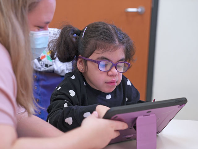 Violet, assisted by a therapist, uses a tablet-like device that helps her communicate.