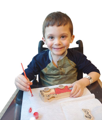Tripp smiles while working on a painting activity. He is sitting in a wheelchair.