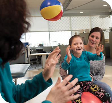 Physical therapist Lizzie Neighbors (right) helps Caetlyn balance on a therapy ball while Caryn and Caetlyn toss a beach ball back and forth during physical therapy. 