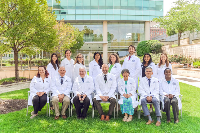 Neurodevelopmental Disabilities Residency Program faculty and trainees in a group photo. Individuals in the front row are seated, with those in the back row standing behind them. The image is taken in Kennedy Kreger's therapy garden.