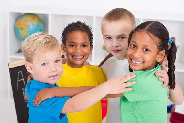 A group of preschool students smile while putting their hands on each other's shoulders and standing in a circle.