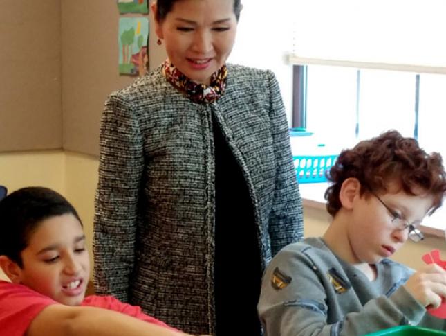 Yumi Hogan, former first lady of Maryland, stands behind two students as they work at their desks.