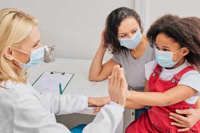 A child with her mother wearing protective face masks at an appointment with a doctor, a woman who is also wearing a face mask. 