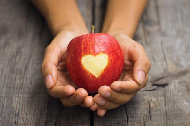 Two hands cusp a red apple with an engraved heart.