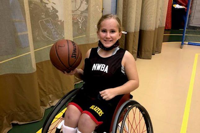 Liza, a Bennett Blazer adaptive athlete, holds a basketball on a basketball court.