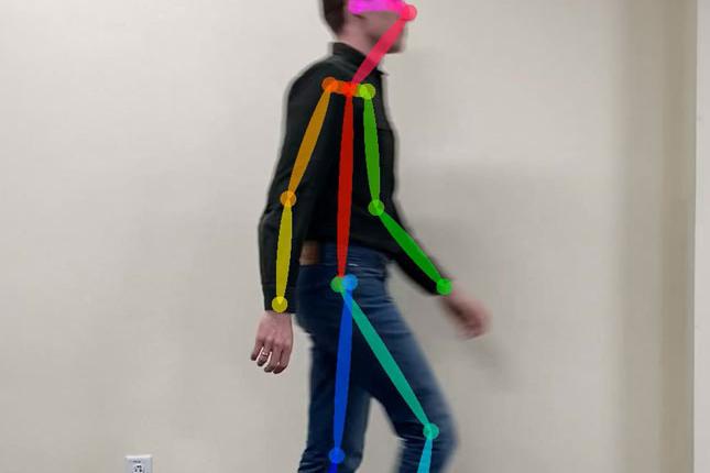 A man walks against a blank wall. Colorful lines are shown over his body, helping researchers analyze his walking and gait. 