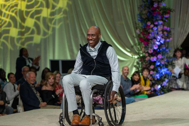 A man in a mobility device smiles on the runway during the 4th Annual Fall Fête. 