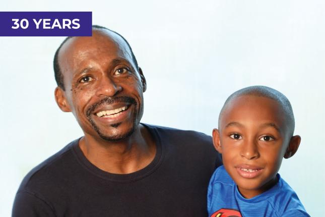 A father and son smile for the camera. The son is about 5 years old and appears to be wearing a Superman T-shirt.