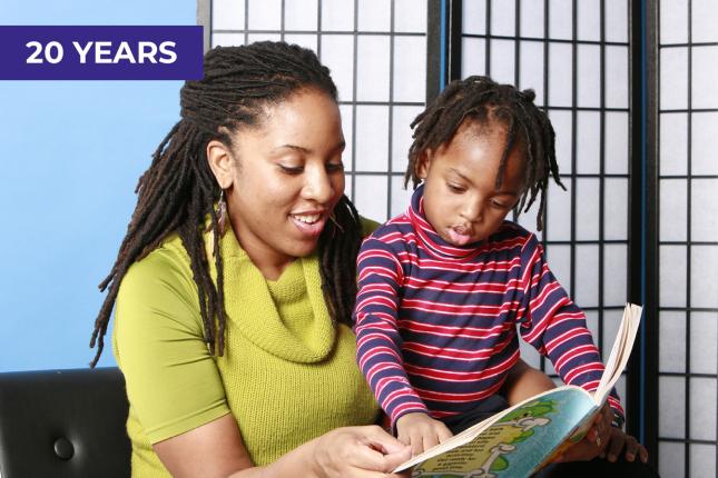 A young woman reads to a little boy, who points to something on the page of the book.