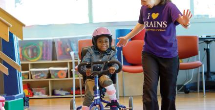 A Phelps Center patient rides a tricycle while her therapist walks along side.