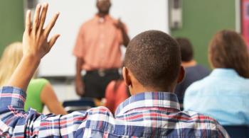 A photo of a student sitting in class, raising his hand and being called on by the teacher