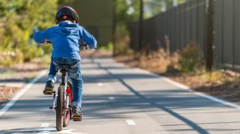 A photograph of a boy riding a bike along a sidewalk