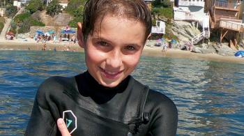A photo of Brayden in a wetsuit, posing in front of an ocean