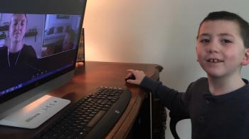 A photo of a Kennedy Krieger student sitting in front of a computer during a virtual school lesson