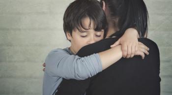 Sad child hugging his mother against a light brick background