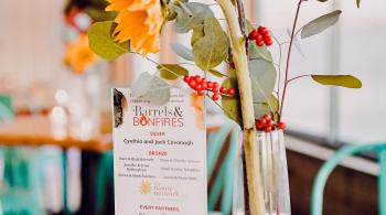 A vase with flowers and plants in it, next to a card that reads Barrels & Bonfires.